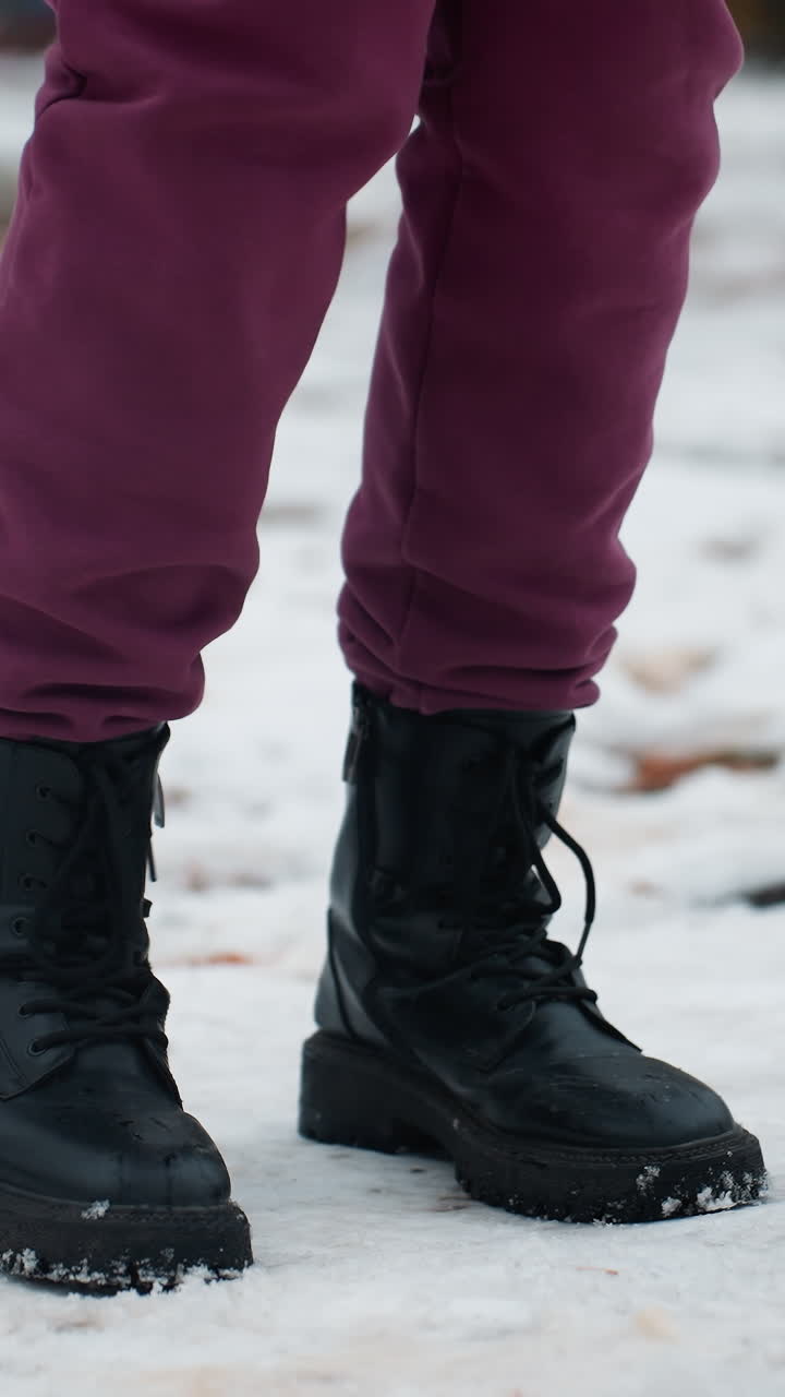 vista lateral de una persona con botas negras saltando de derecha a izquierda en un terreno cubierto de nieve, el entorno de invierno destaca el movimiento, el calzado robusto y la atmósfera estacional nítida