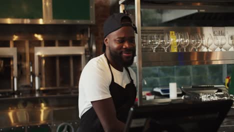 A-Black-person-works-dancing-in-a-doner-market-against-the-backdrop-of-a-barbecue.-A-man-in-a-black-apron-and-white-t-shirt-is-happy-at-his-favorite-job