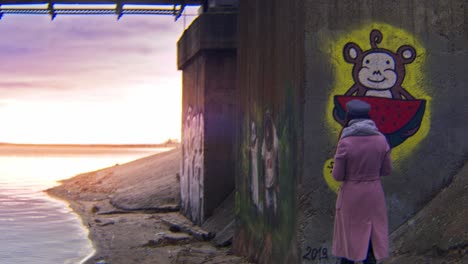 mujer observando el arte del graffiti junto a un río al atardecer