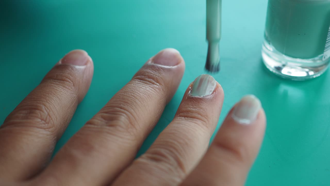 mujer pintando sus uñas con esmalte de uñas verde claro