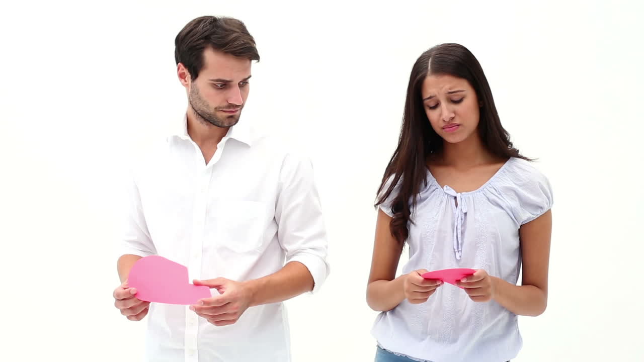 una joven y triste pareja sosteniendo dos mitades de un corazón roto.