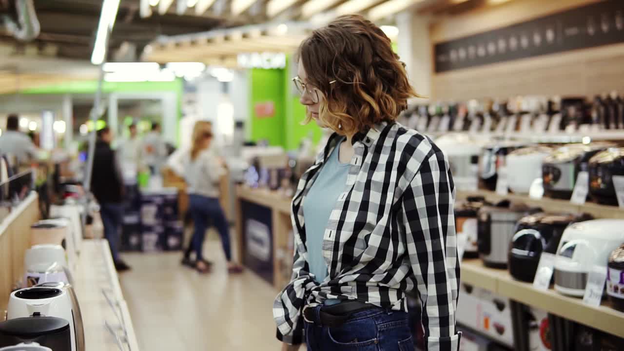 긴 양말을 신은 매력적인 소녀가 스케이트보드를 들고 해가 질 때 쇼핑몰 근처 주차장에 있는 쇼핑 카트에 앉아 있는 여자 친구와 이야기를 나누고 있습니다.