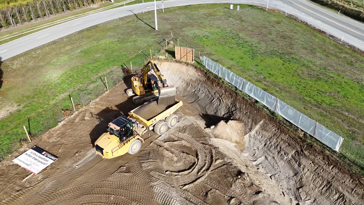 Drone captures excavator and dump truck moving soil at a construction site in Cromwell, New Zealand. Bright daylight enhances visibility