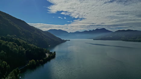 una toma aérea de seguimiento de una vista rústica de un paisaje montañoso junto al lago en austria