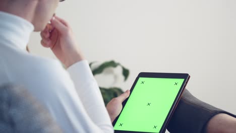 person with leg injury relaxing at home and using a tablet with a green screen