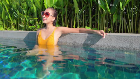 American-Woman-Inside-Swimming-Pool-Water-Leaning-on-the-border-edge-of-the-Pool-in-the-tropical-Hotel-lounge-in-Miami,-static-slow-motion