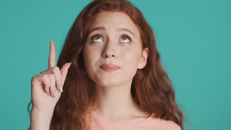 redheaded girl in front of camera on turquoise background.