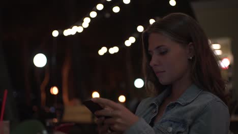 woman using a smartphone and having coffee at night cafe.