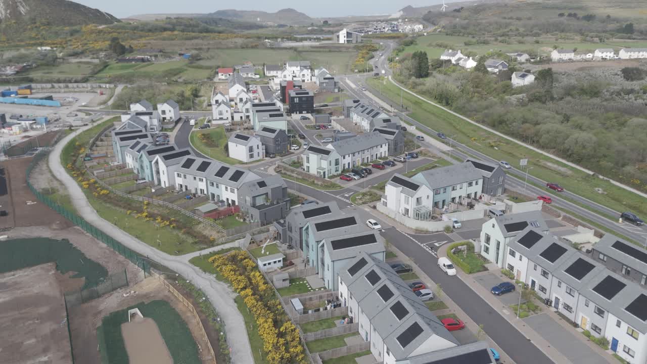 Aerial pull-out of modern solar-roofed housing estate with curved streets, white-and-grey facades and landscaped verges showcasing sustainable suburban design and energy-efficient living