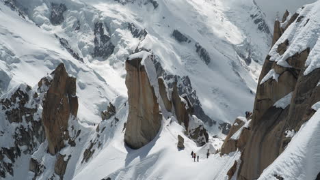 alpinisti e alpinisti sulla neve sotto le ripide scogliere rocciose delle alpi francesi, chamonix, francia