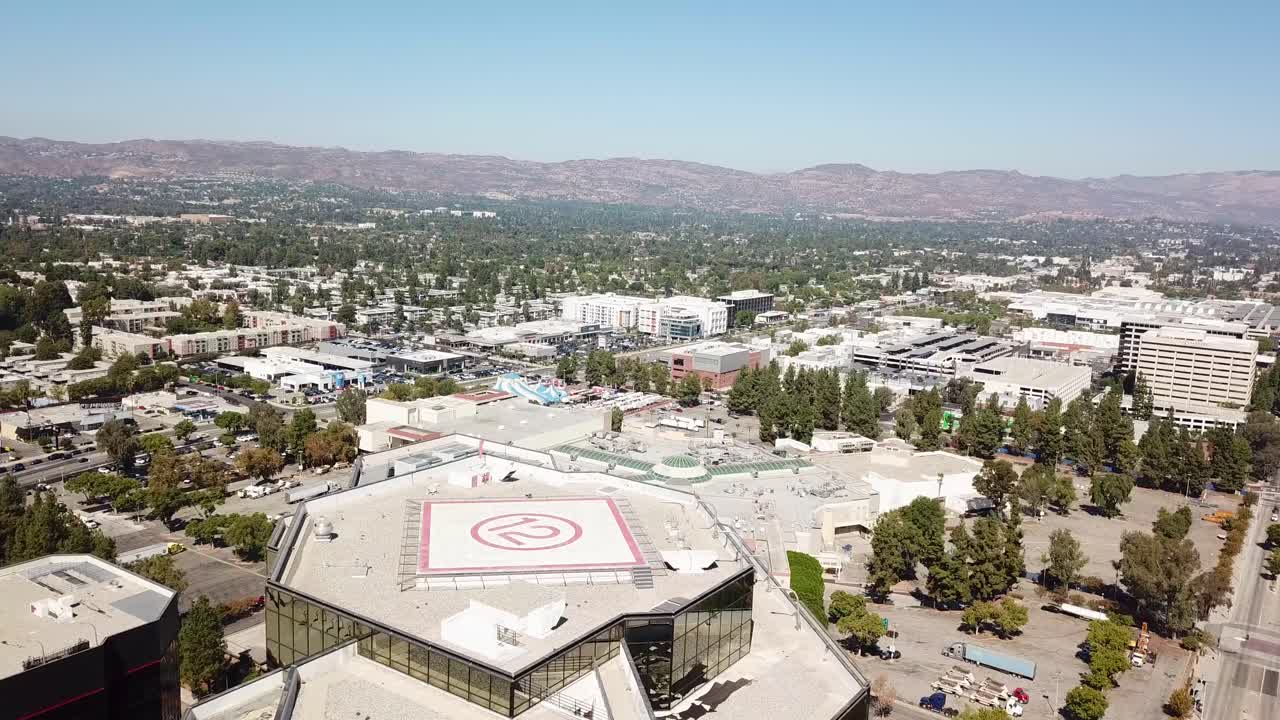 Aerial flyover high-rise Buildings with helipad in Woodland Hills, Los Angeles. Sunny day in american suburb town with main highway and green forest landscape of USA. Wide shot. California, LA.