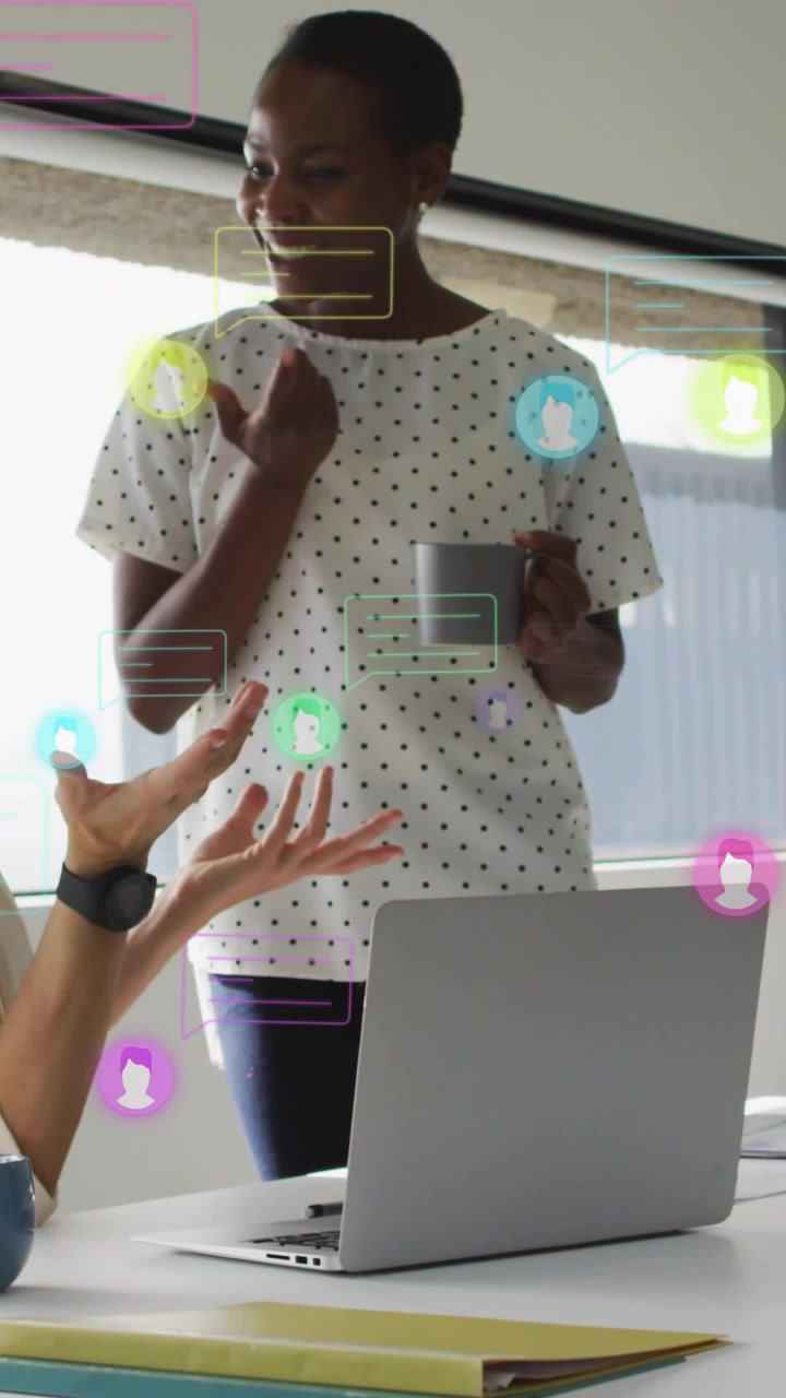 Video verticale: Donna che si unisce a un tavolo, rispondendo ai gesti di un collega, discutendo di lavoro tramite laptop, UI di chat.