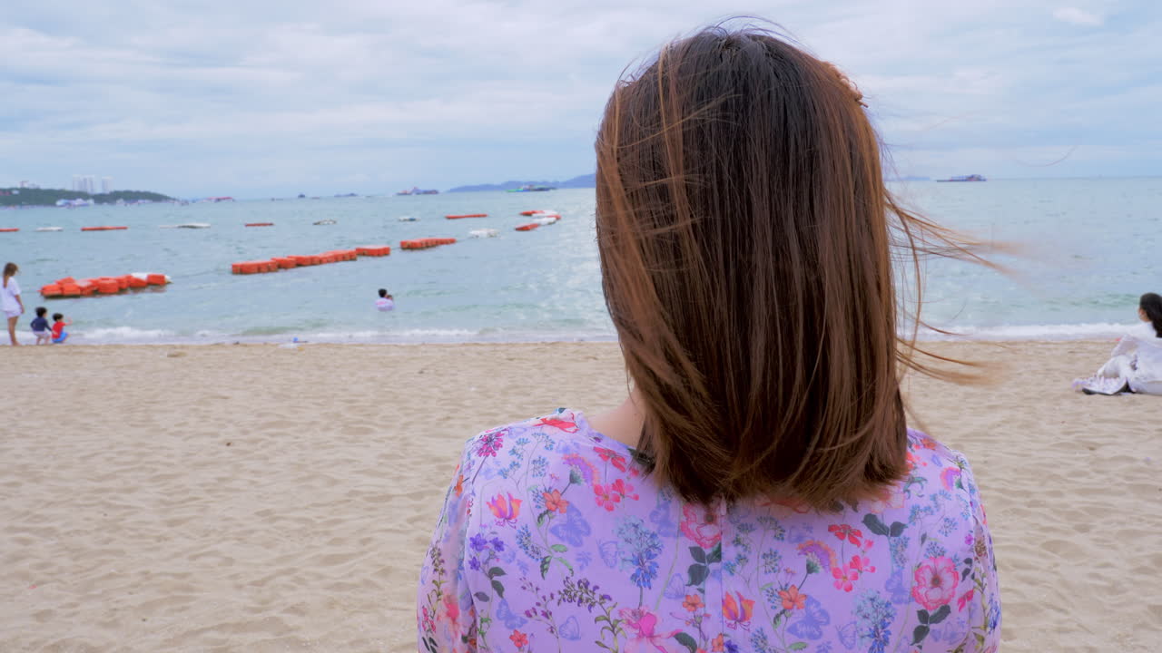A woman looking at the other beachgoers who are swimming and sitting at Pattaya beach in Chonburi province in Thailand