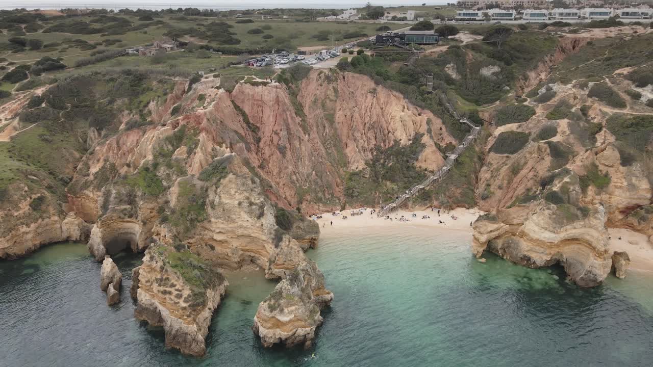 Aerial drone moves out from sandy beach, dramatic cliffs, and turquoise water near Lagos in Algarve