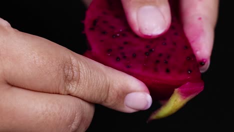 fingers delicately hold and manipulate vibrant dragon fruit slices against a dark background.