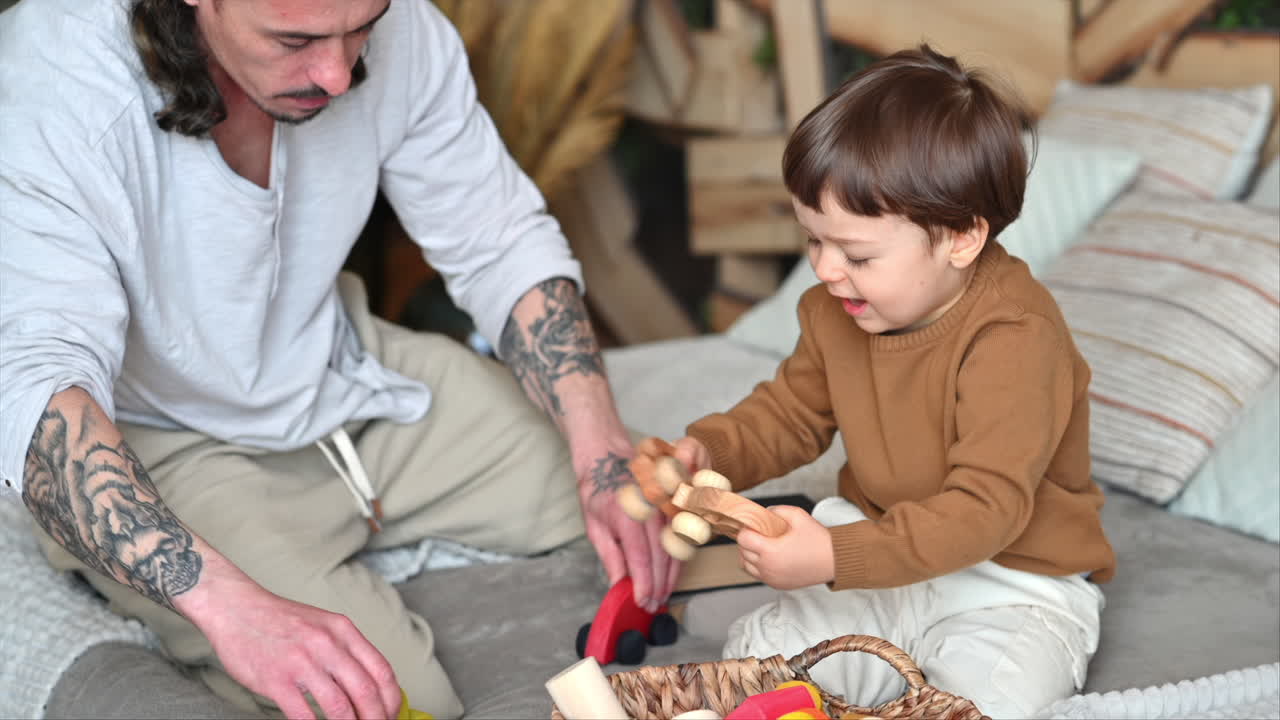 Father playing with his son with colourful, ecological wooden toys from a basket on the bed