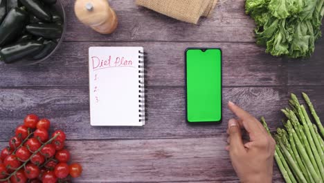 top view of man's hand holding smart phone with fresh vegetable on table