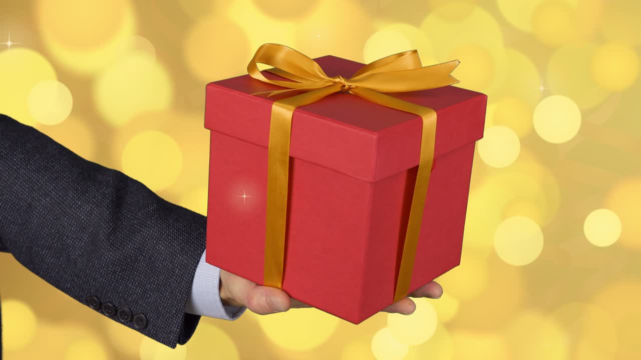 hombre mano masculina sostiene caja de regalo roja con arco de oro. celebrar la víspera presente caja de regalos. hombre caucásico en traje clásico. fondo abstracto flash dorado parpadeando y brillo círculo luces bokeh. cerrado.