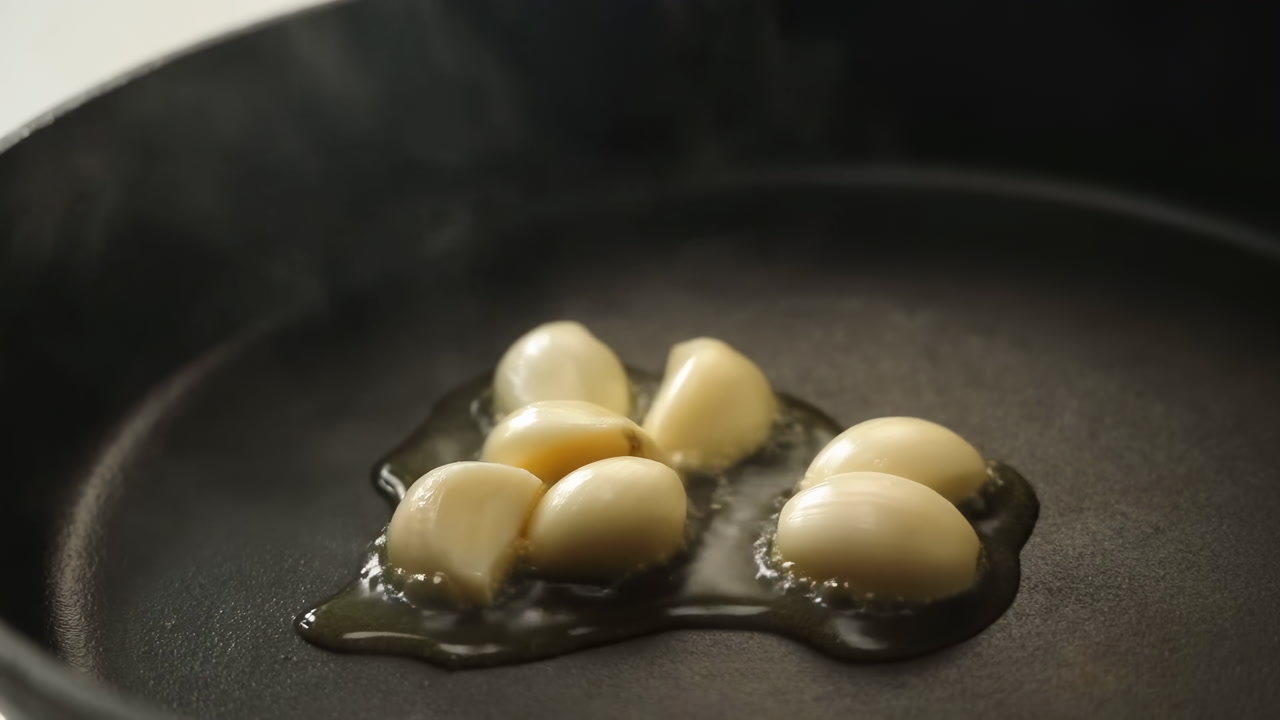 Garlic Cloves Sizzling In Oil In Black Skillet With Gentle Steam Rising, Closeup Of Golden Edges Forming