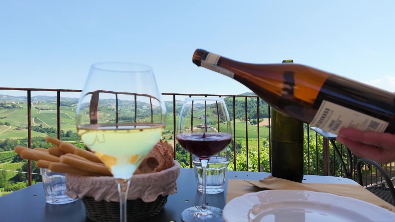 Una mano versa vino rosso in un bicchiere su un balcone con vista su dolci colline verdi