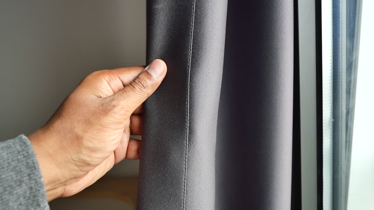 사람이 창문에서 손으로 어두운 회색 커튼을 열고