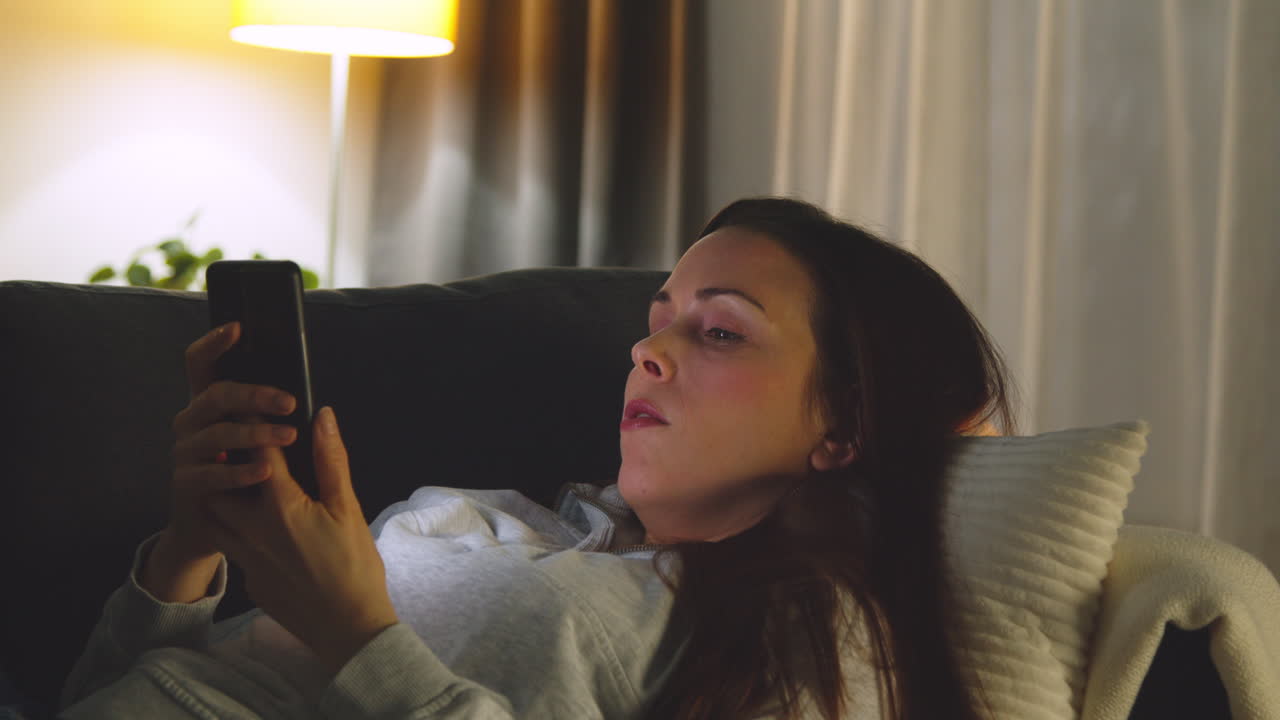 Woman Lying On Sofa At Home At Night Streaming Or Looking At Online Content On Mobile Phone 2