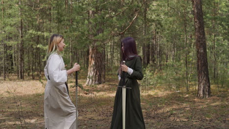 girls in long vintage medieval dresses hold swords in forest