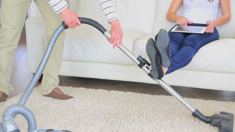 man hoovering carpet while wife is relaxing on sofa