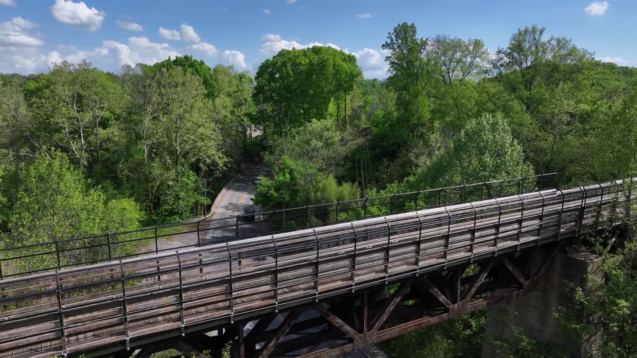Wood bridge and driving cars underpass during sunny day in America. Green spring trees and blue sky. Lynchburg, Virginia.