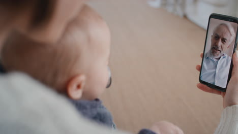 Madre-Y-Bebé-Conversando-Por-Video-Con-El-Abuelo-Usando-Un-Teléfono-Inteligente-Saludando-Al-Recién-Nacido-Disfrutando-De-La-Conexión-Familiar-4k