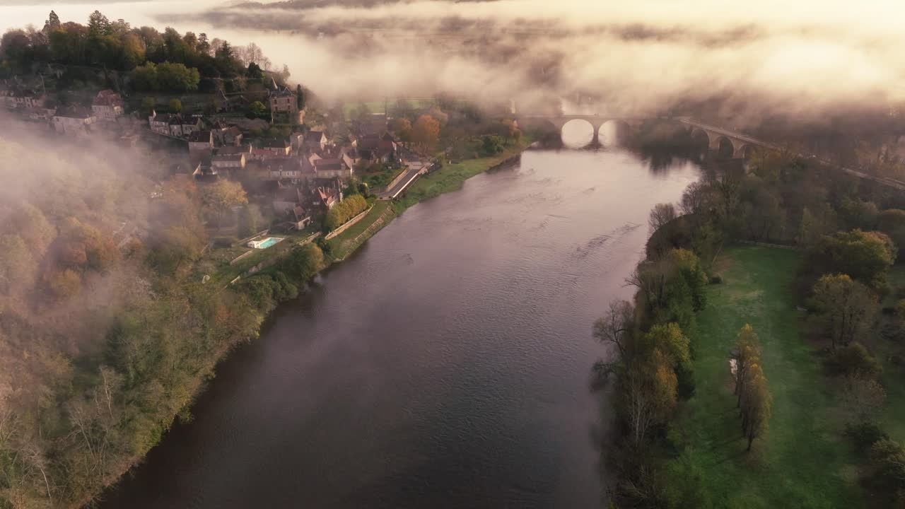 Filmato drone dall'alto che segue la curva del fiume Dordogna vicino a Limeuil, Francia. Una fitta nebbia mattutina avvolge la riva sinistra mentre una luce soffusa colpisce l'acqua e gli alberi.