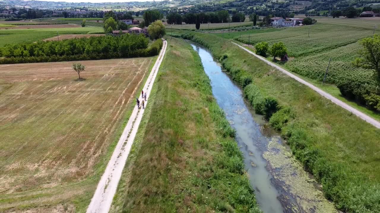 toma aérea de un grupo de ciclistas pedaleando por un camino de tierra cerca de un pequeño río