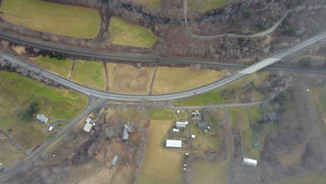 Birdseye-view-of-Vermont-landscape-with-road,-cars,-train-track,-barn,-houses,-and-autumn-colors