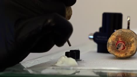 foto de mano en cámara lenta de la mano de un artista del tatuaje sumergiendo su pistola de tatuaje en un pequeño recipiente de tinta negra para trabajar en un cliente