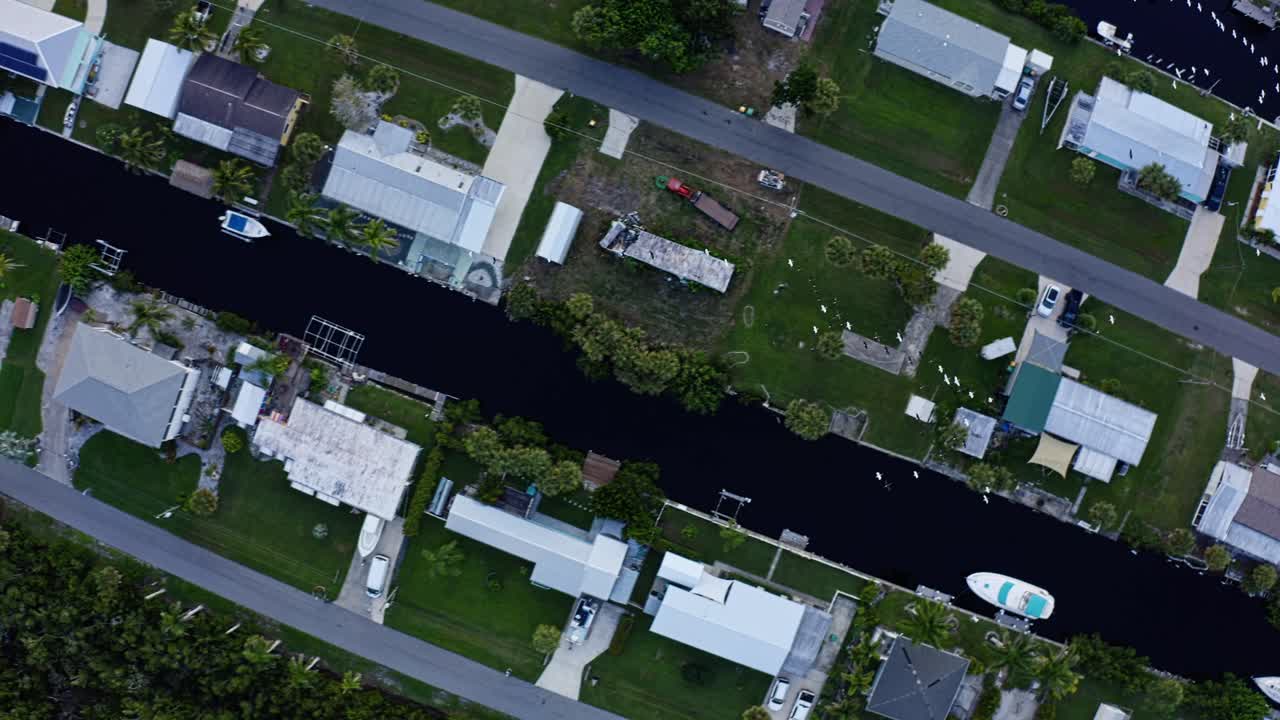Waterfront homes sit along a calm canal bordered by green lawns and docks, where small boats rest beside the houses in a peaceful suburban setting