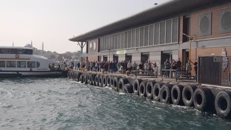 people walking on a dock with a ferry in the background