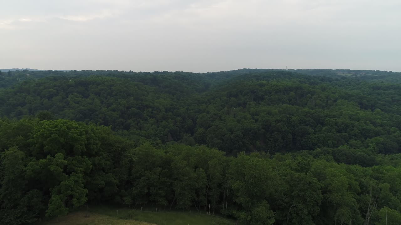 A slow forward aerial establishing shot of the Pennsylvania wooded countryside. A small farm or field below.