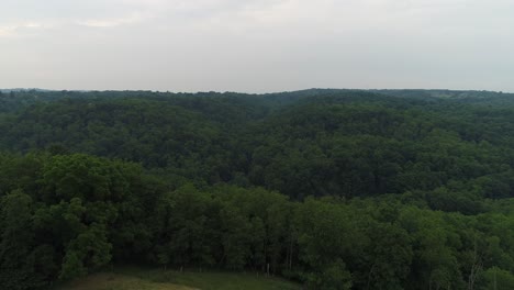 a slow forward aerial establishing shot of the pennsylvania wooded countryside. a small farm or field below.