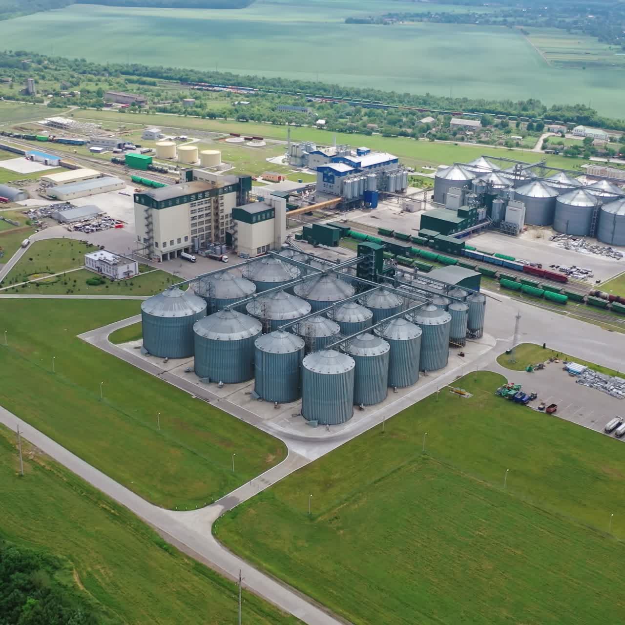 Modern factory among fields. Grain elevators for keeping agricultural products. Grain storage tank in the countryside. Aerial view.