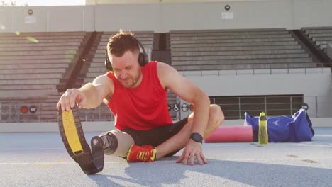 Caucasian-disabled-male-athlete-with-running-blade-wearing-headphones-and-stretching