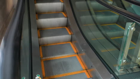 first-person perspective showing a close view of two escalators, one going up and the other going down. the escalator handrails and steps in a modern indoor setting