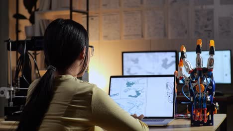 back view of teen asian girl with 3d printing designing a cyborg hand on a laptop at home