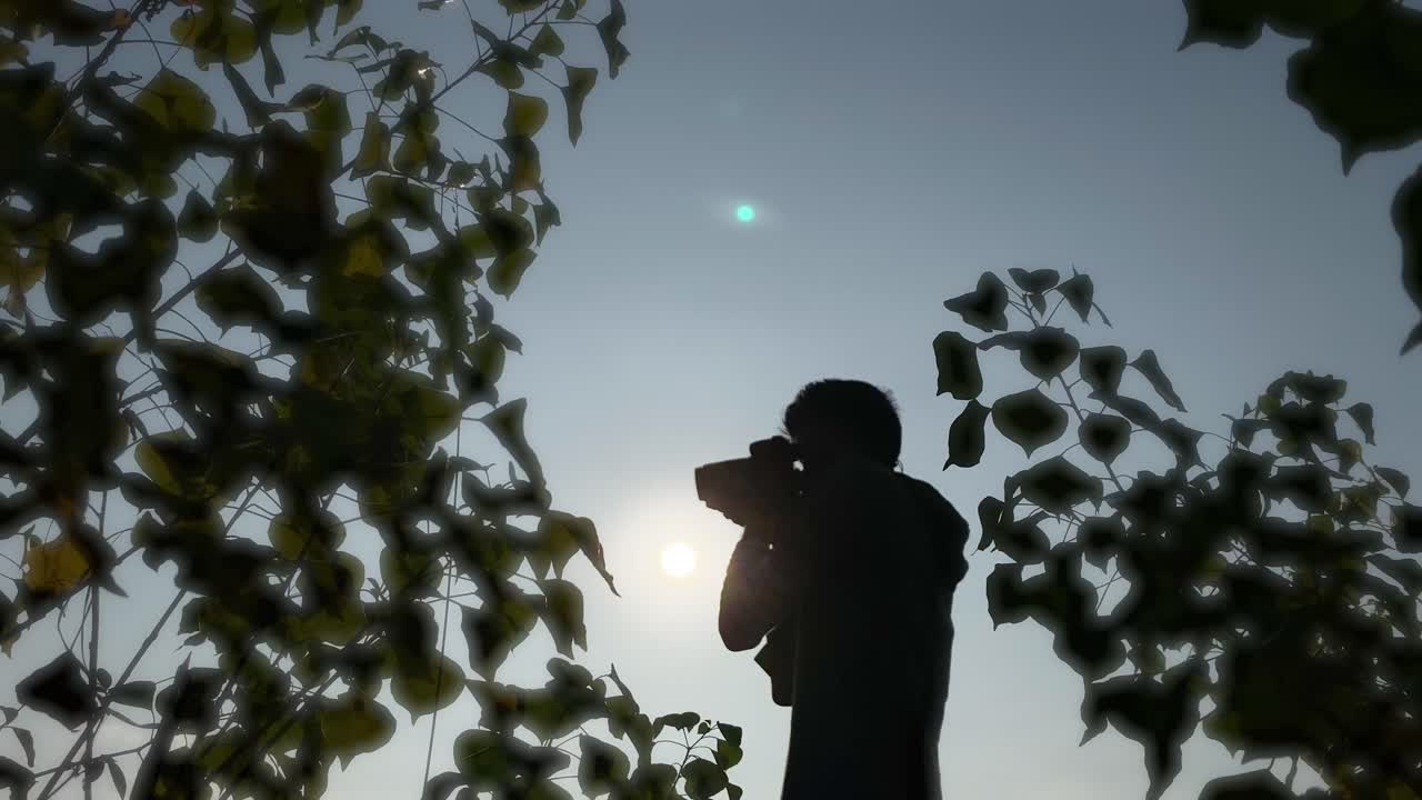 Silhouette of photograher holding DSLR camera, shooting in nature, bright sky