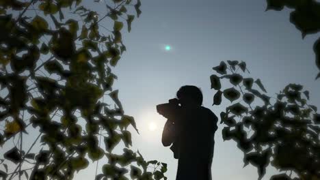 silhouette of photograher holding dslr camera, shooting in nature, bright sky