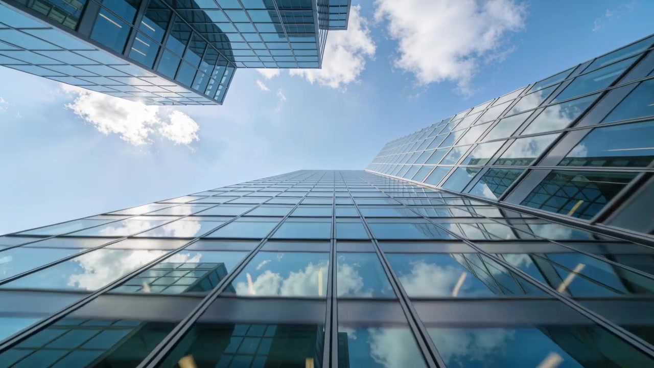 Camera kantelend na kadering op straatniveau, onthult glazen kantoortoren die blauwe luchtwolken reflecteert