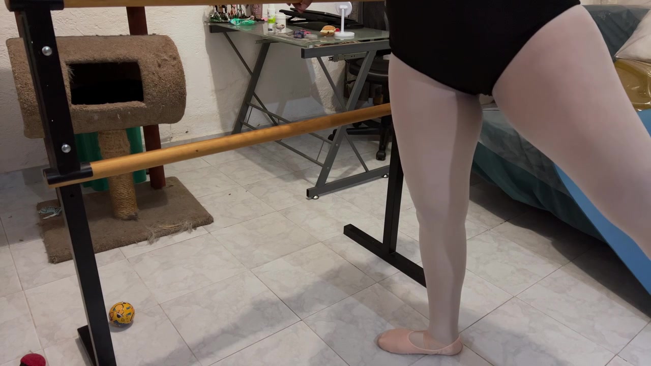 Uma bailarina pratica movimentos graciosos em uma barra de balé doméstica em um ambiente interno casual.
