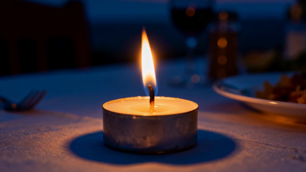Una candela tealight che brucia stabilmente su un tavolo da pranzo, sfarfallando e poi spegnendosi, rilasciando fumo.
