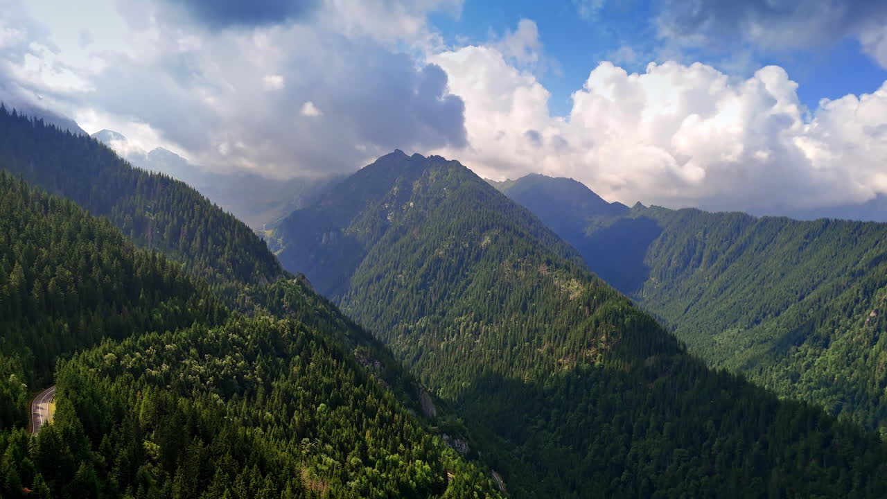 Footage in the mountains covered with evergreen pine tree woods. Clouds float in the sky above the rocks. Romania