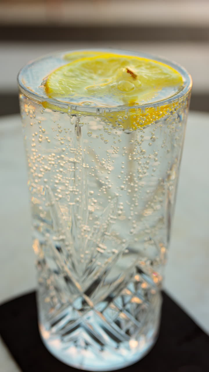 Primo piano di un bicchiere di acqua frizzante con una fetta di limone su un tavolo in una terrazza. Verticale