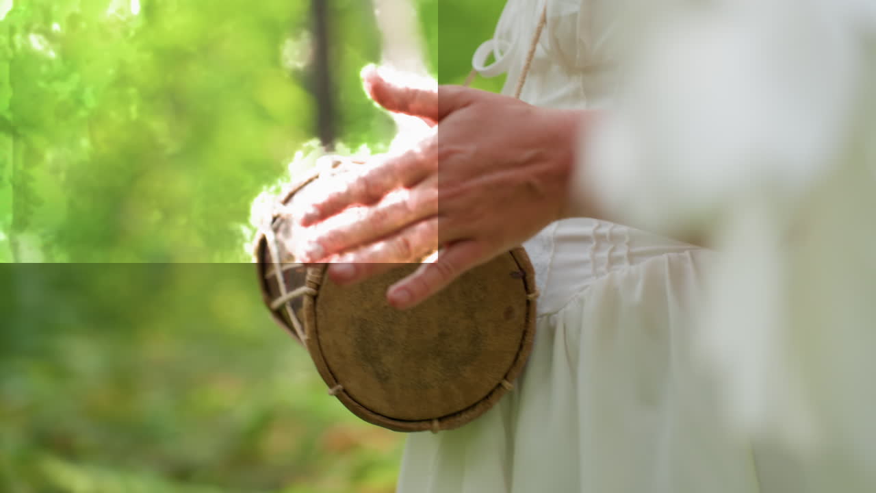Close up of fairy woman in white dress with wings walking in green forest while beating hand drum, soft sunlight on hands and leather skin, gentle rhythm, cultural vibe, peaceful nature mood